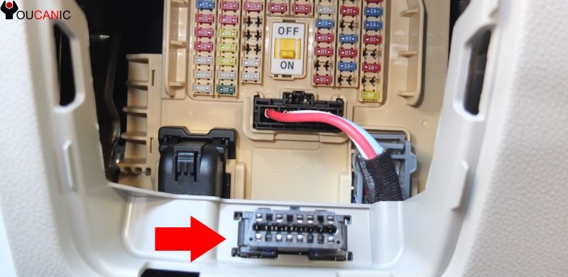 Accessing the OBD2 port under the dashboard of a Kia Optima.